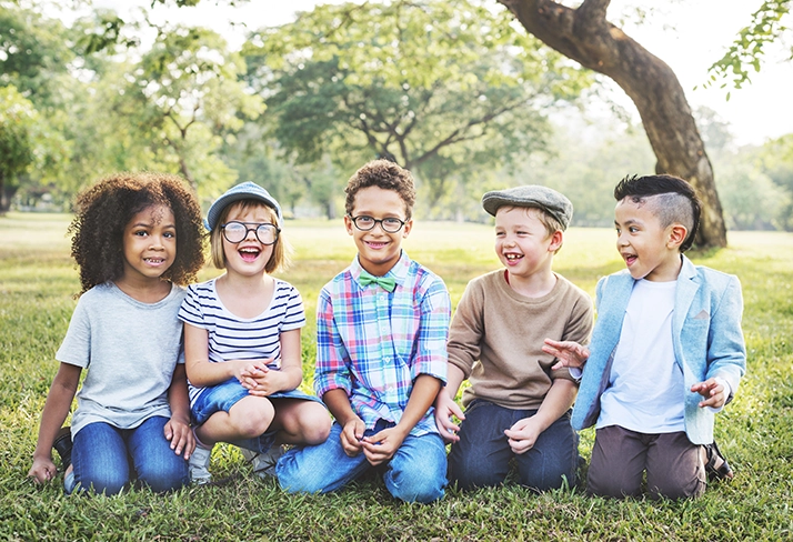 5 kids smiling while sitting in the grass.